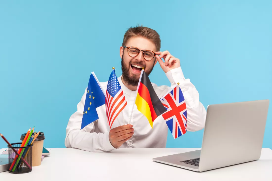 smiling-man-teacher-adjusting-eyeglasses-holding-flags-usa-german-great-britain-europe-countries-advertising-foreign-languages-studying-school-indoor-studio-shot-isolated-blue-background